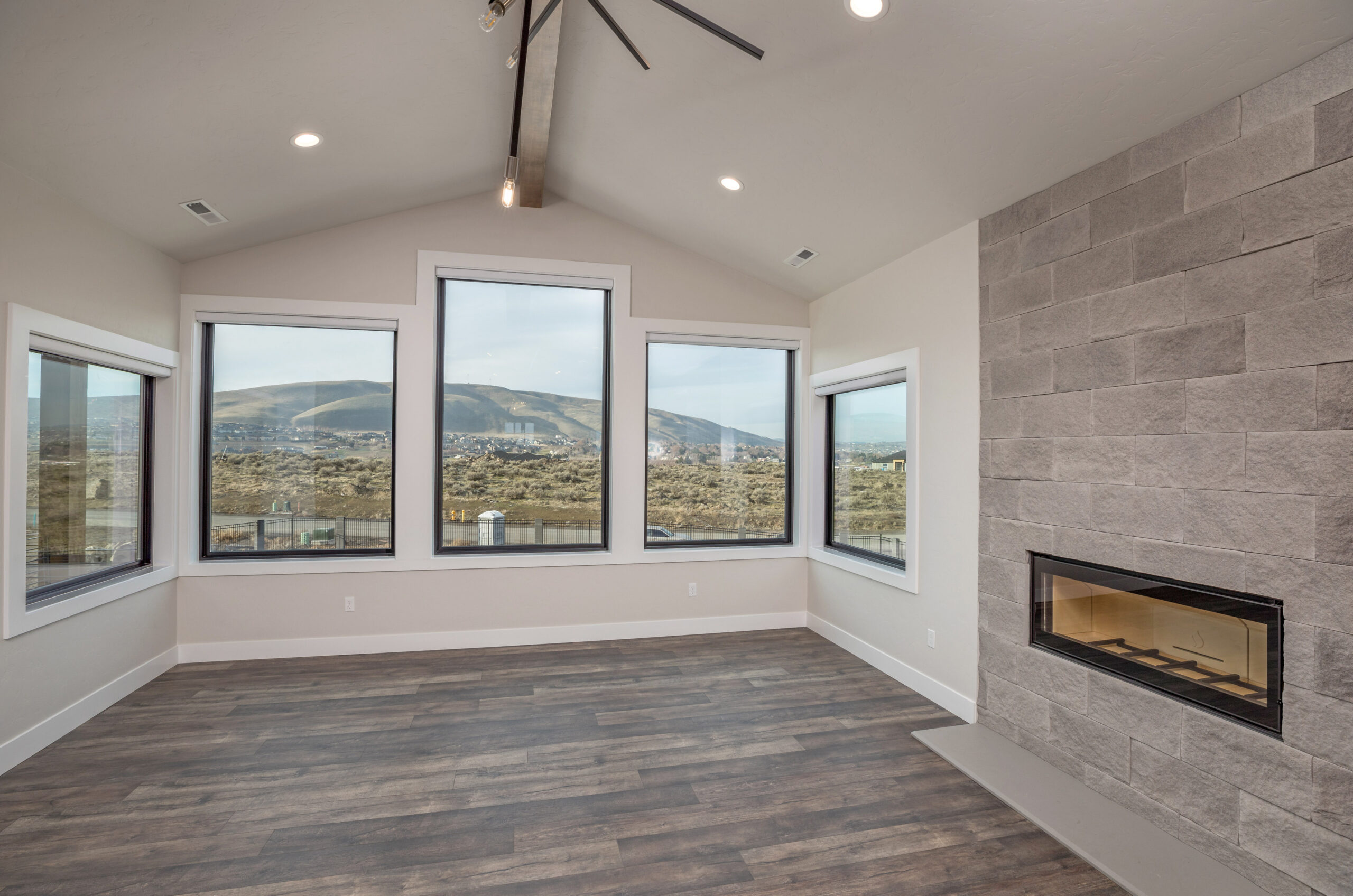 Modern empty family room design with fire place and lot of windows facing a scenic backyard.